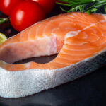 rohes Lachsfilet neben Zitronen und Tomaten