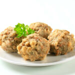 vier Knödel mit einem Balsamicoblatt auf einem kleinen Teller
