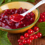 Rote Grütze in einer Schüssel mit Löffel und Waldbeeren und Blättern an der Seite