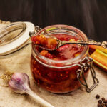 Chutney in einem Glasbehälter mit Knoblauch, Pfeffer & Paprika auf einem Tisch