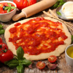 Pizzateig mit Tomatensauce, Eigelb, Gewürzen, Tomaten, Basilikum und Oliven auf einem Tisch